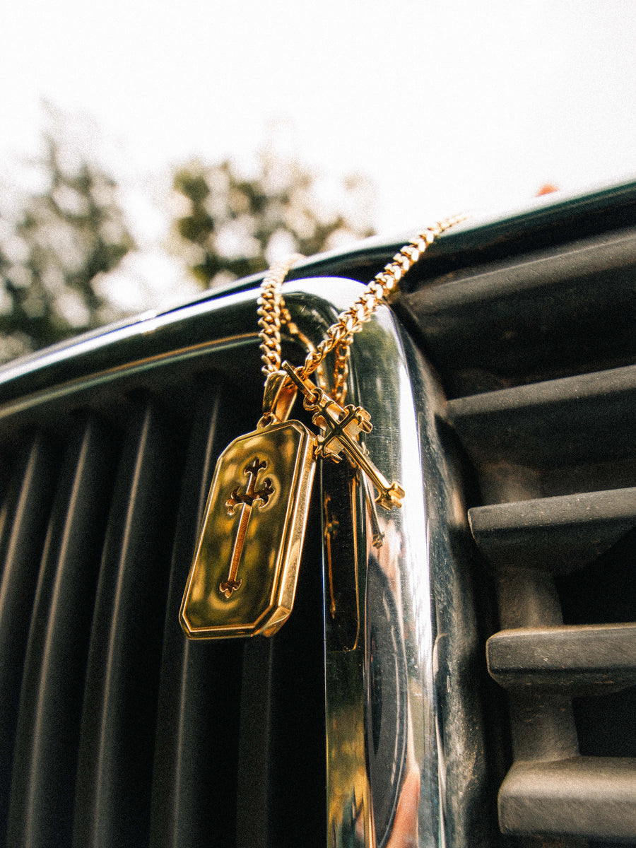 Cross Stack Necklace in gold resting on a car grille